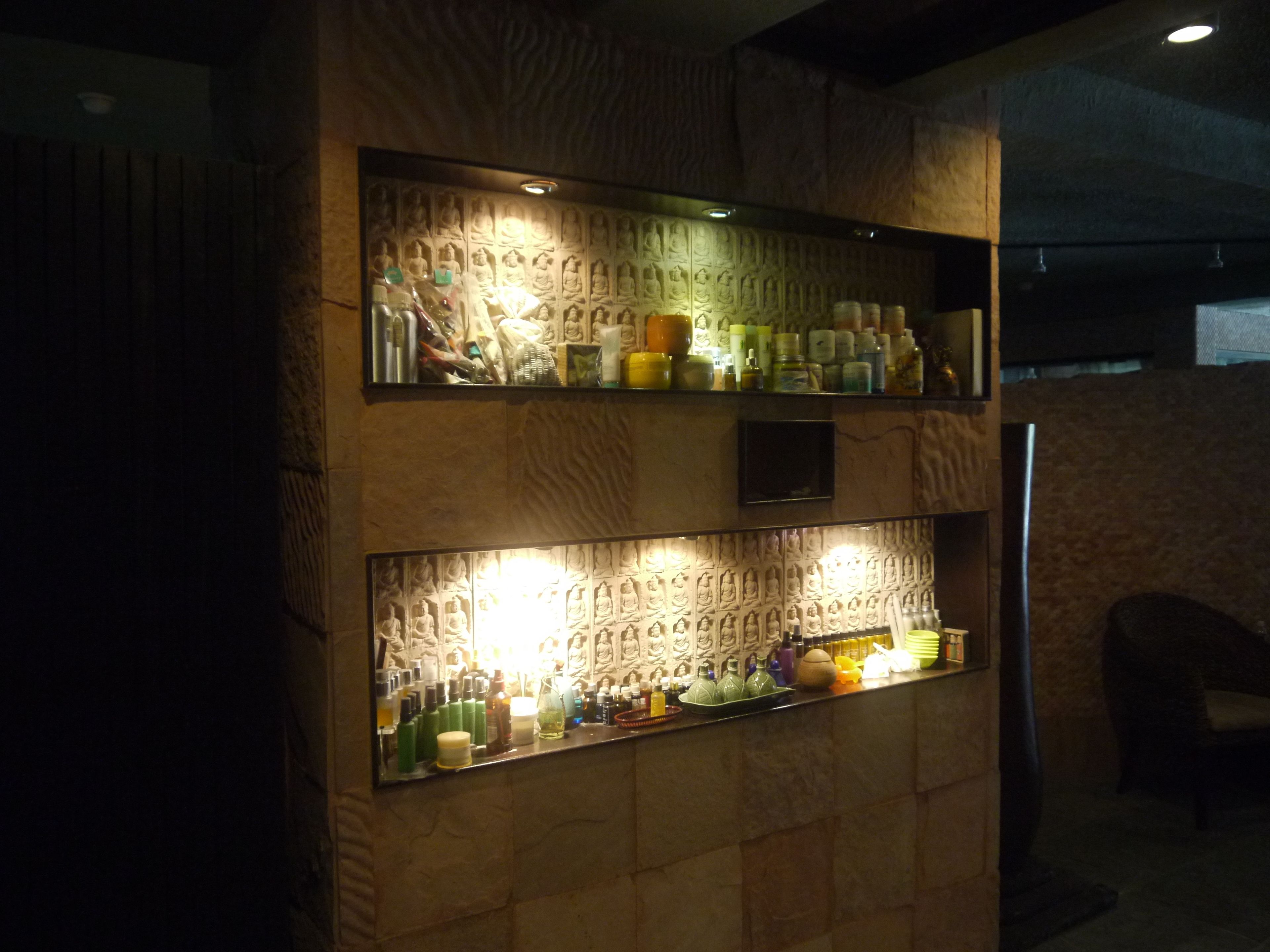 A bar area with shelves displaying bottles and glasses, a textured wall with relief sculptures, and a chair to the right.