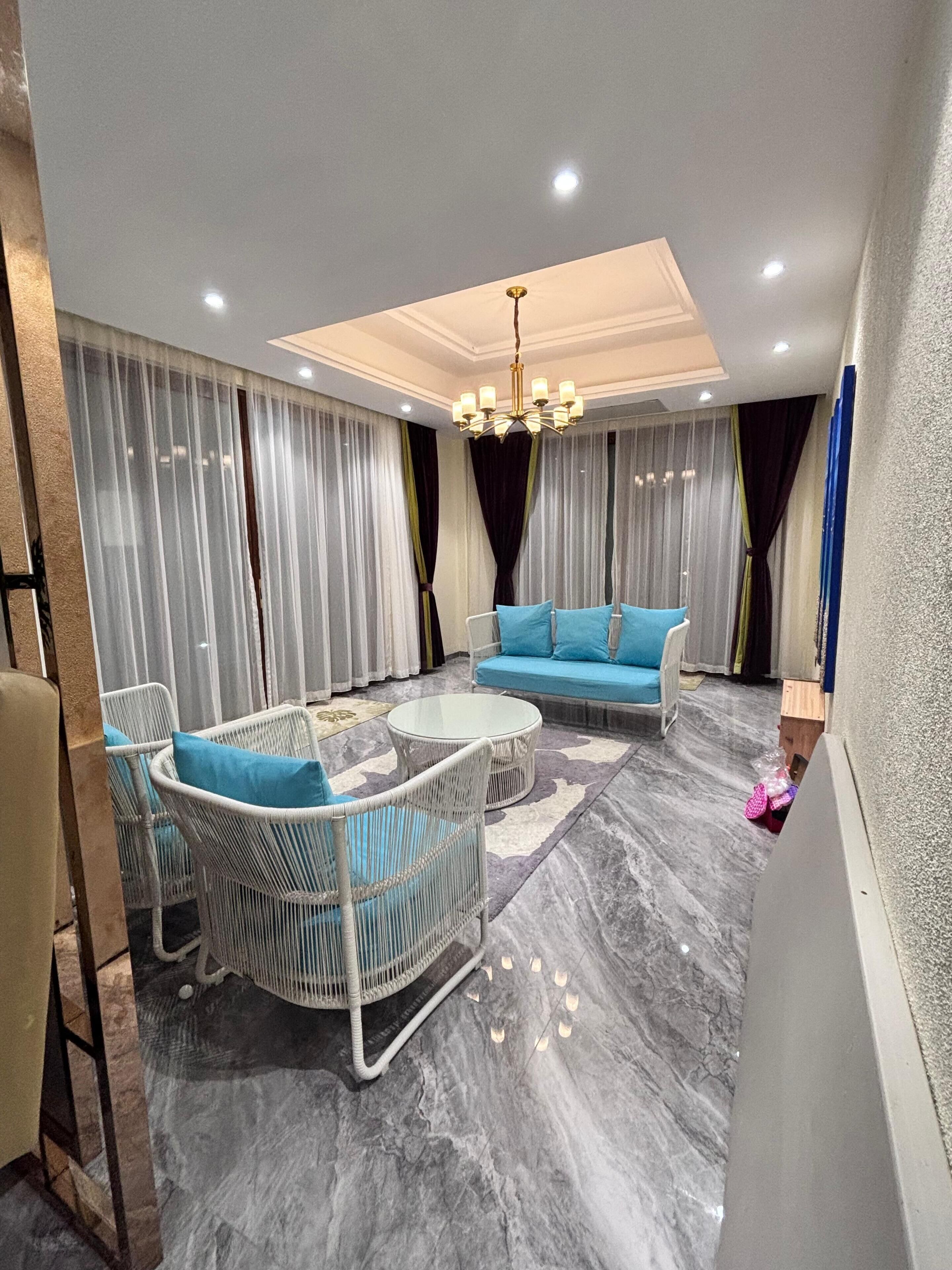 A modern living room with a sofa, two armchairs, a coffee table, and a chandelier.