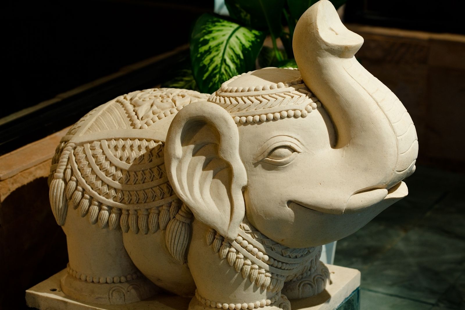 Una detallada escultura de elefante con intrincados grabados y detalles en cuentas, ubicada sobre un pedestal.