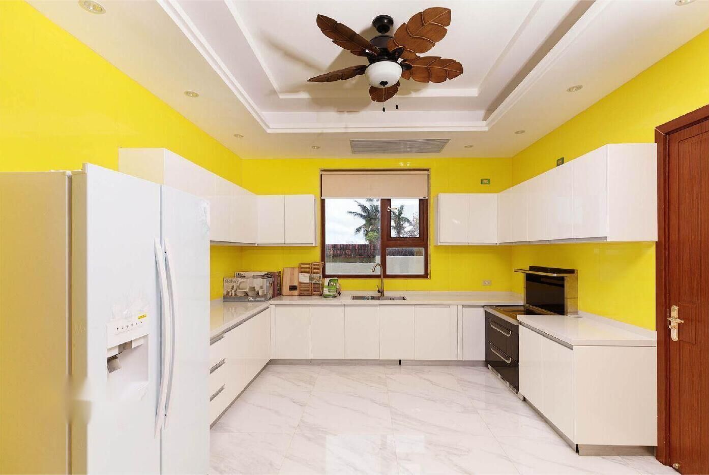 A kitchen with white cabinets, a white refrigerator, a wooden door, and a ceiling fan.