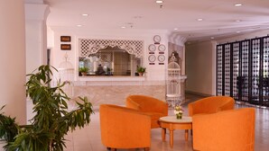Eine Lobby mit Empfangsschalter, einer Wand mit Uhren und einer Sitzecke mit orangefarbenen Stühlen.