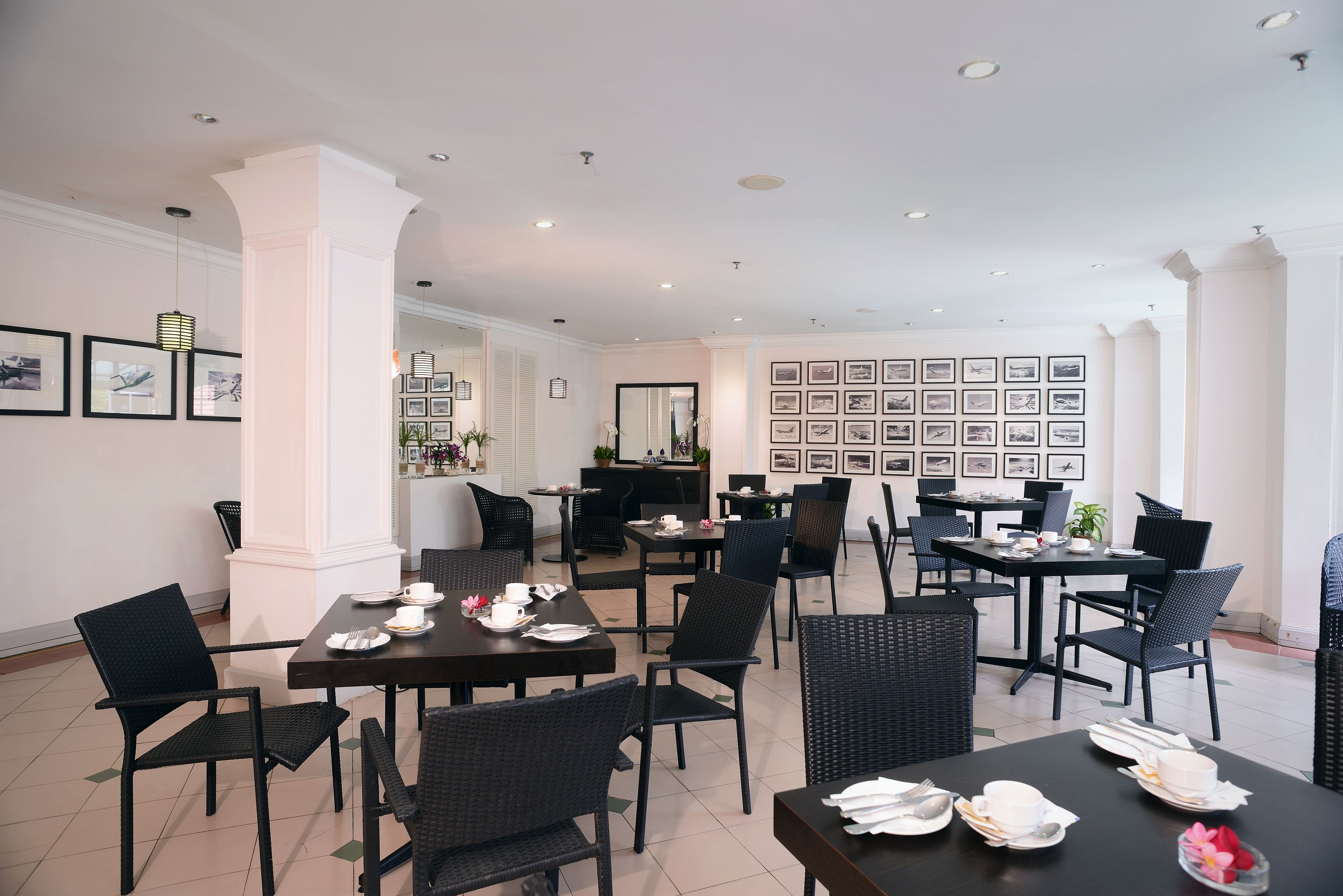 A hotel dining area with multiple tables and chairs, a reception desk, and framed pictures on the walls.