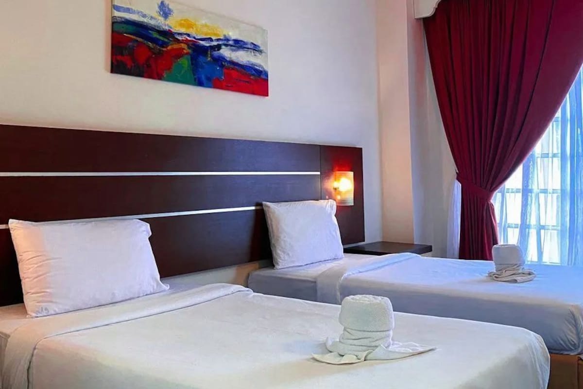 Une chambre d’hôtel avec deux lits, un tableau au mur et une fenêtre avec des rideaux.