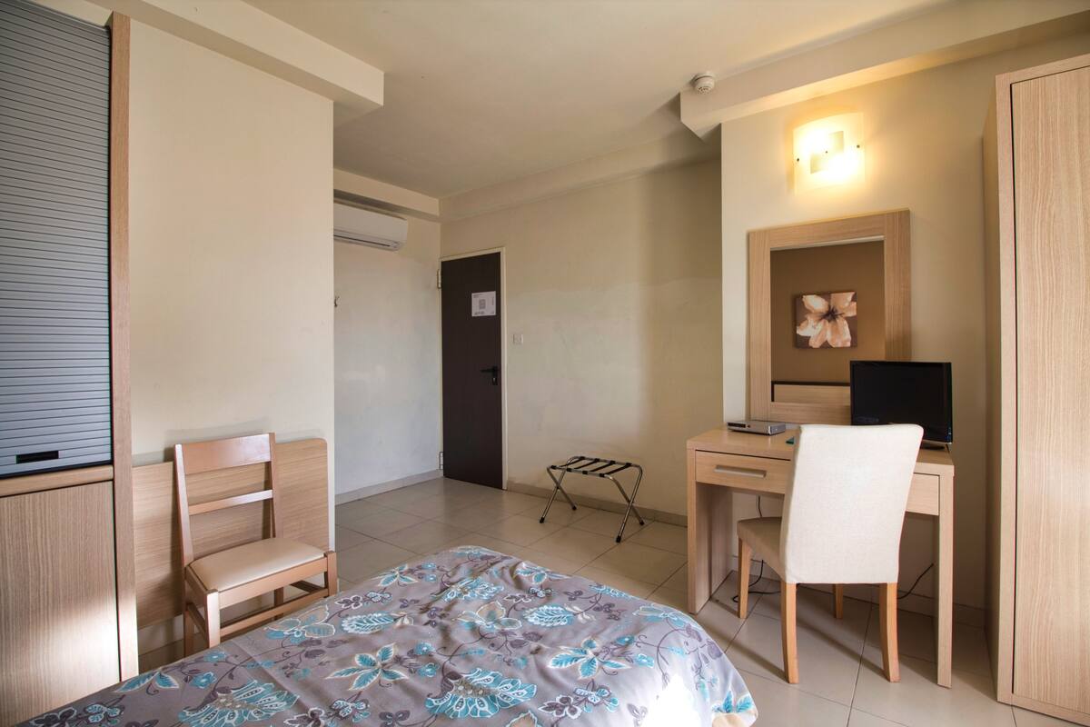 Quarto com uma cama, escrivaninha com computador, cadeira e guarda-roupa.