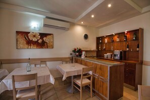 A dining area with a wooden table and chairs, a small bar counter, and a wall-mounted clock. - Hotel Kappara (San Gwann)