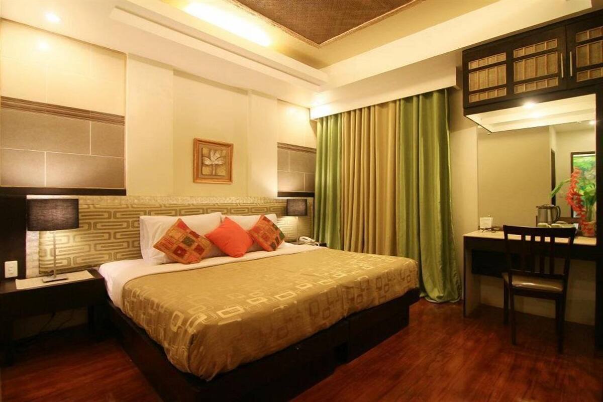 A hotel room with a large bed, a desk with a chair, a nightstand, and a wardrobe.