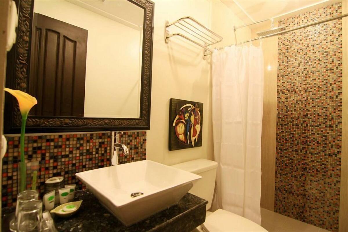 A bathroom with a large mirror, a white sink, a toilet, and a shower curtain.