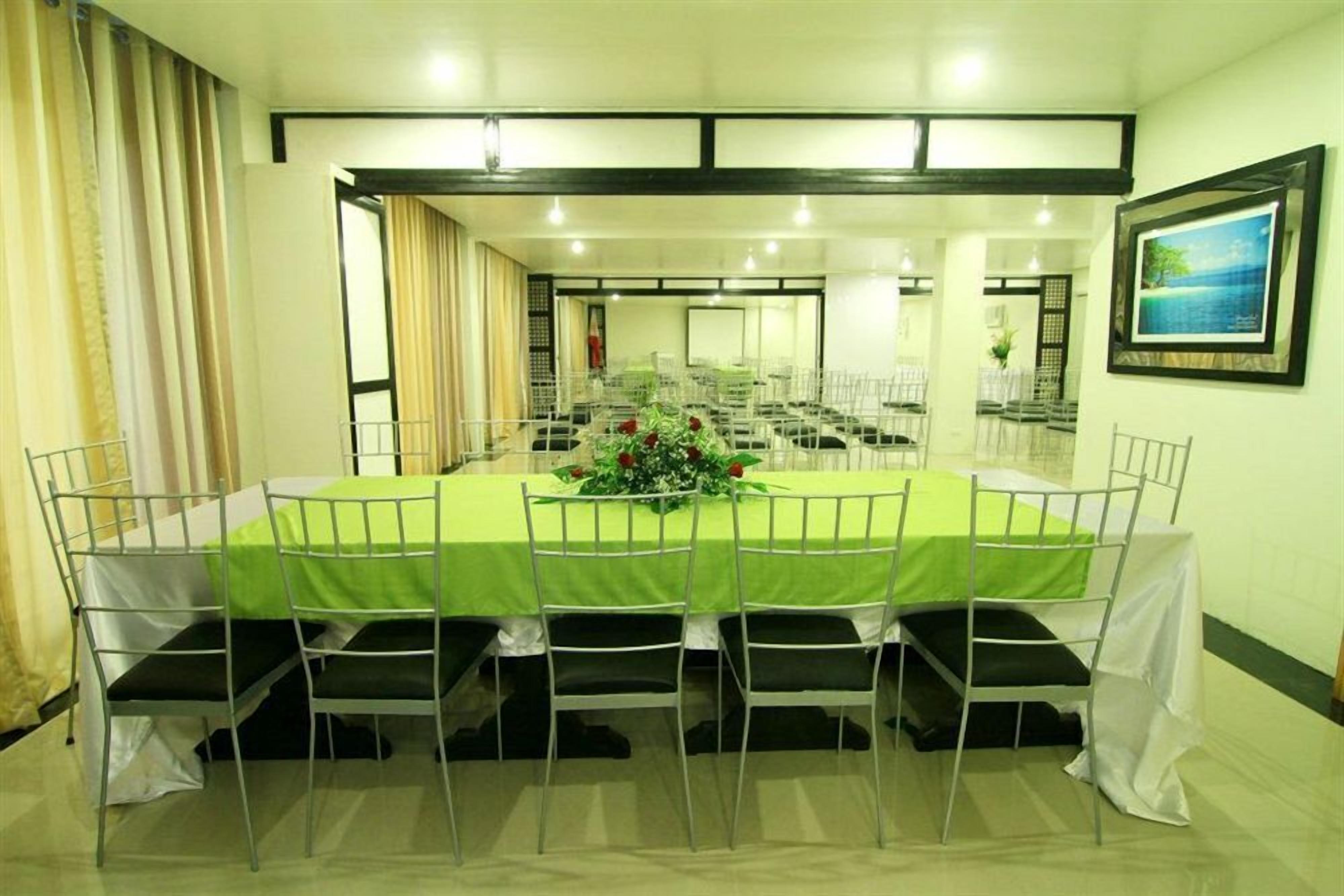 Una sala de conferencias con una larga mesa, sillas blancas y un mantel verde.