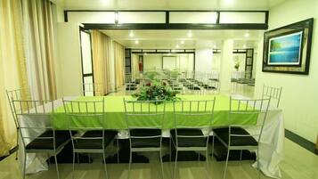Una sala de conferencias con una larga mesa, sillas blancas y un mantel verde.
