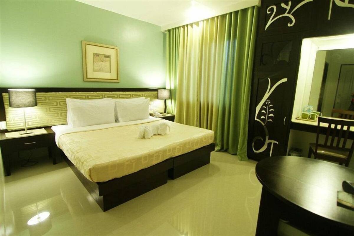 A hotel room with a bed, bedside tables, a mirror, a chair, and a small table.