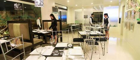 A modern dining area with tables set for service, a waiter attending to a table, and a waiter preparing another table.