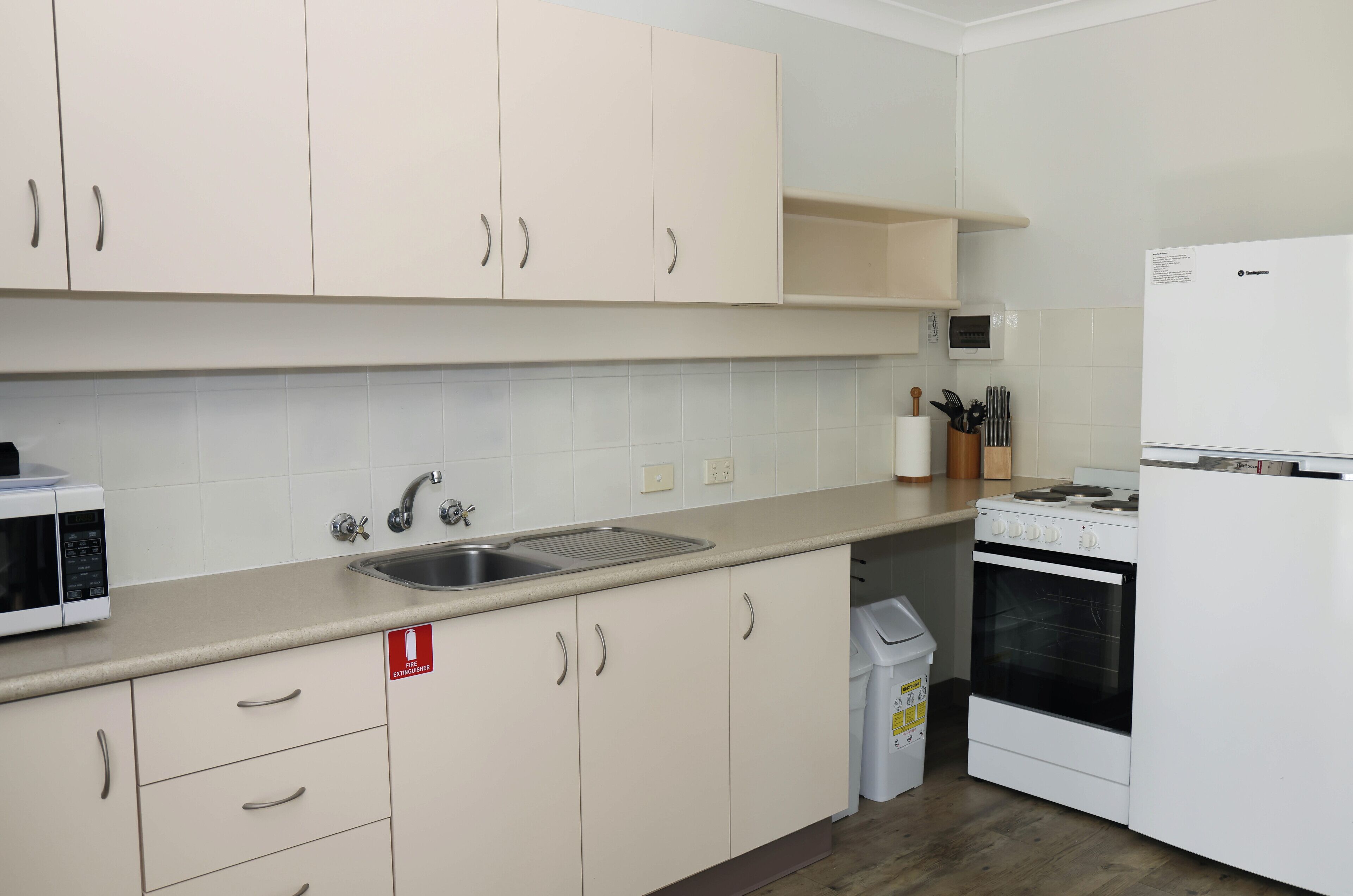 Una cocina moderna con armarios blancos, un lavamanos de acero inoxidable, un microondas, una estufa y un refrigerador.