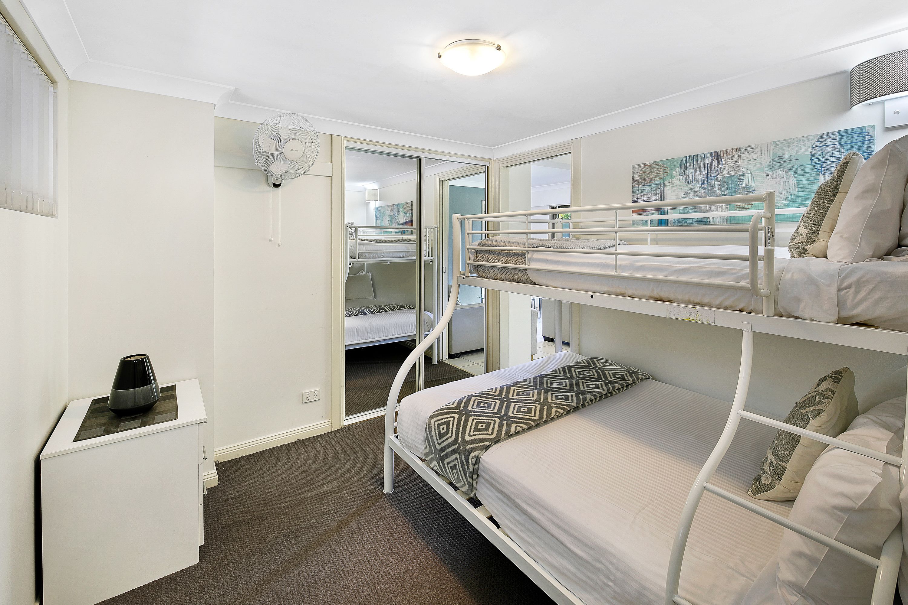 A bunk bed room with a desk and a fan.