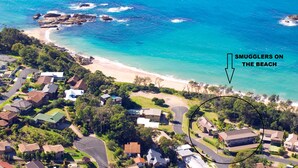 Vista aérea de una zona residencial costera con casas, una playa y un área señalada con un círculo que dice 'SMUGGLERS ON THE BEACH'.