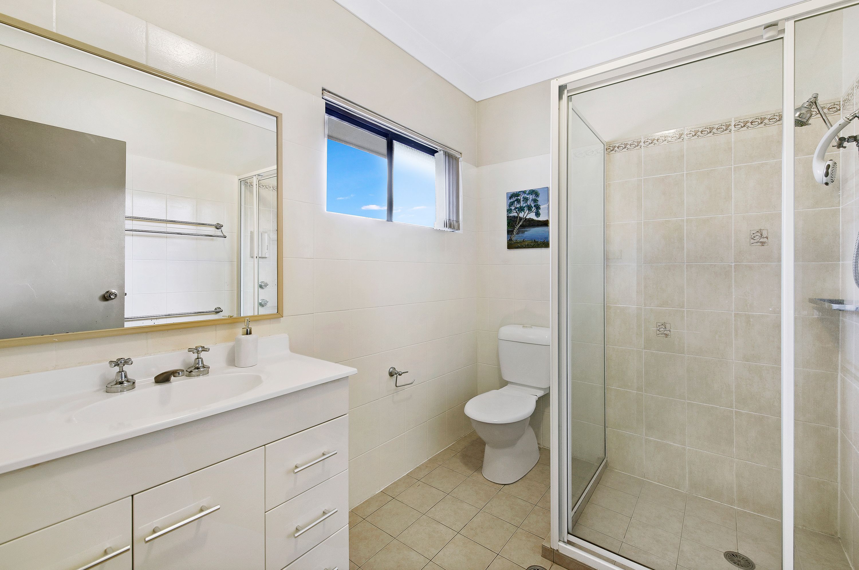 Een badkamer met een grote spiegel, toilet, douchecabine en raam.