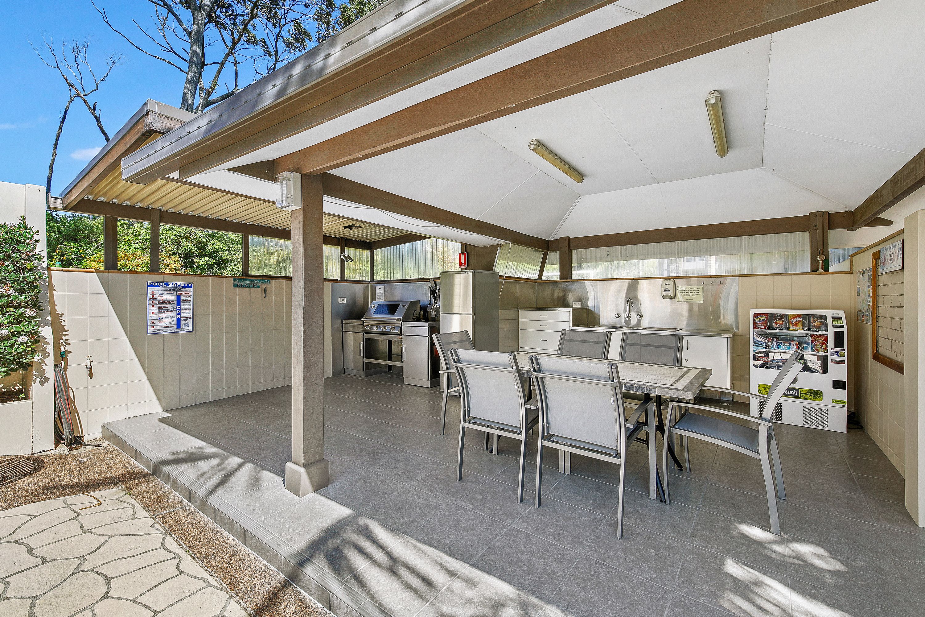 An outdoor patio area with a covered seating area, a vending machine, and a pool safety sign.