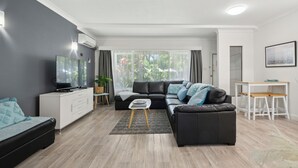 Una sala de estar moderna con un sofá modular, una mesita de centro, un mueble blanco y un televisor.