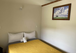 Ein Hotelzimmer mit einem Bett, einem Landschaftsbild und einer weißen Wand.