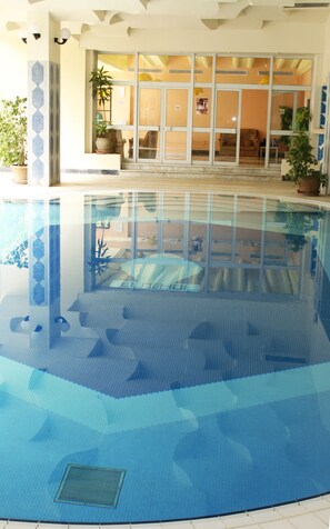 An indoor swimming pool with clear water, a tiled floor, and a view of the lobby area with a sofa and potted plants. - Primasol El Mehdi (Mahdia)
