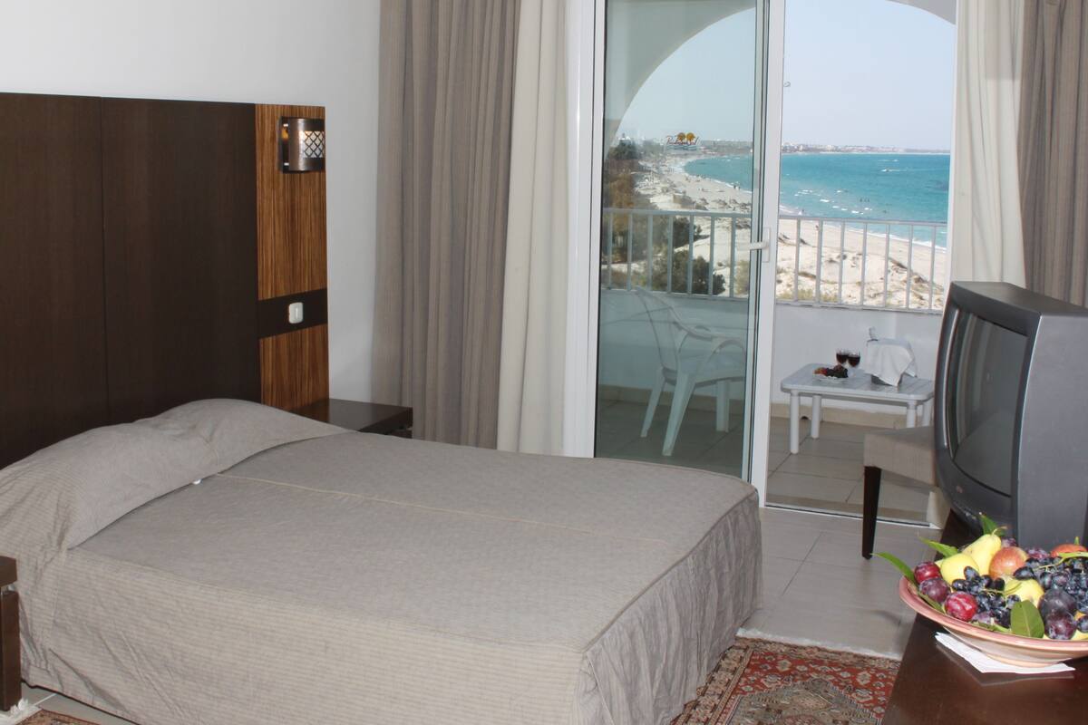 Habitación de hotel con cama, televisor y balcón con vista a la playa.