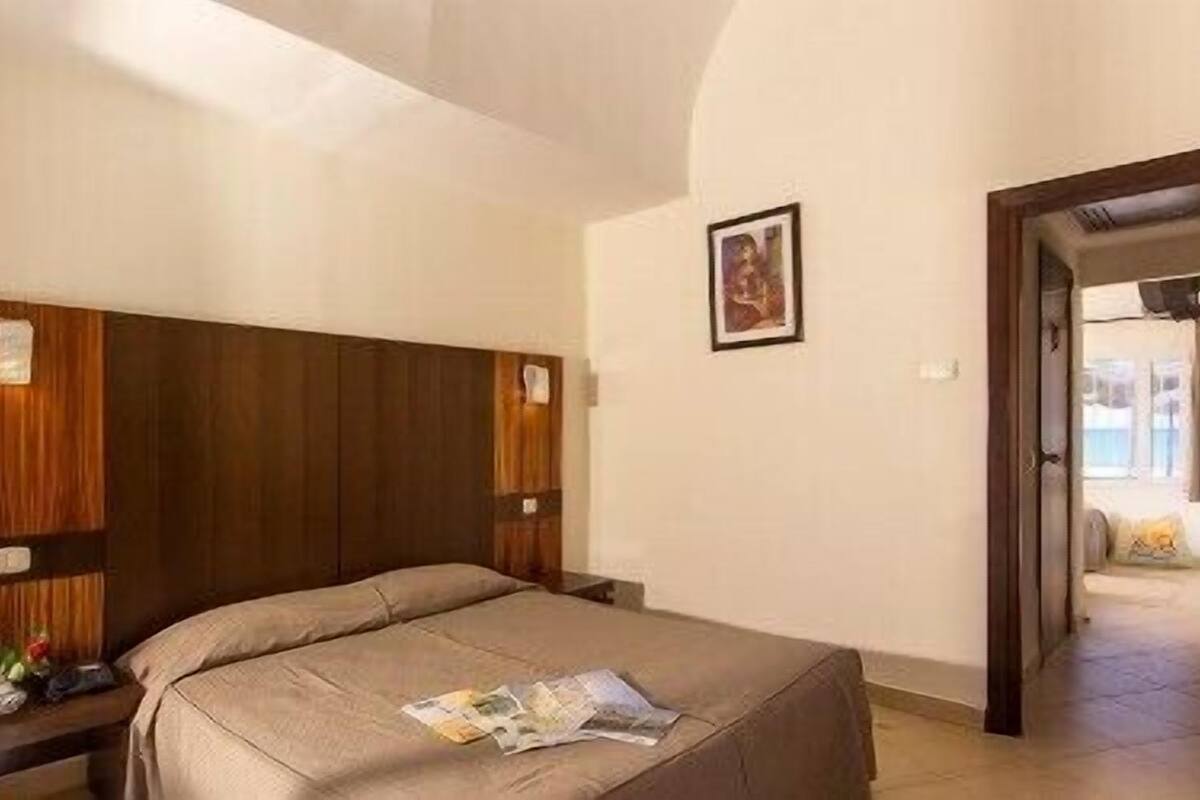 Un dormitorio con cabecera de madera, cama con colcha color beige y un cuadro enmarcado en la pared.