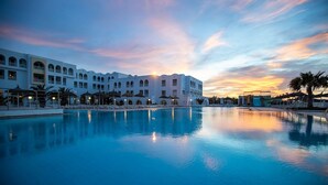 A hotel with a large pool, white architecture, and a sunset sky.