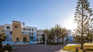 A hotel with a central courtyard, palm trees, and a clear sky.