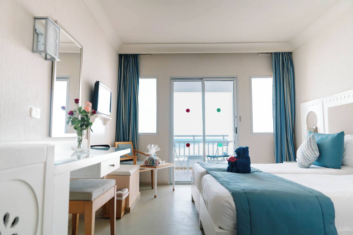 A hotel room with a bed, desk, chair, and a view of the outside.