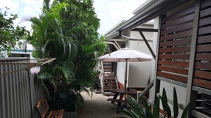 A patio area with a wooden bench, a table with an umbrella, and a variety of plants. - Brisbane Street Studios (Annerley)
