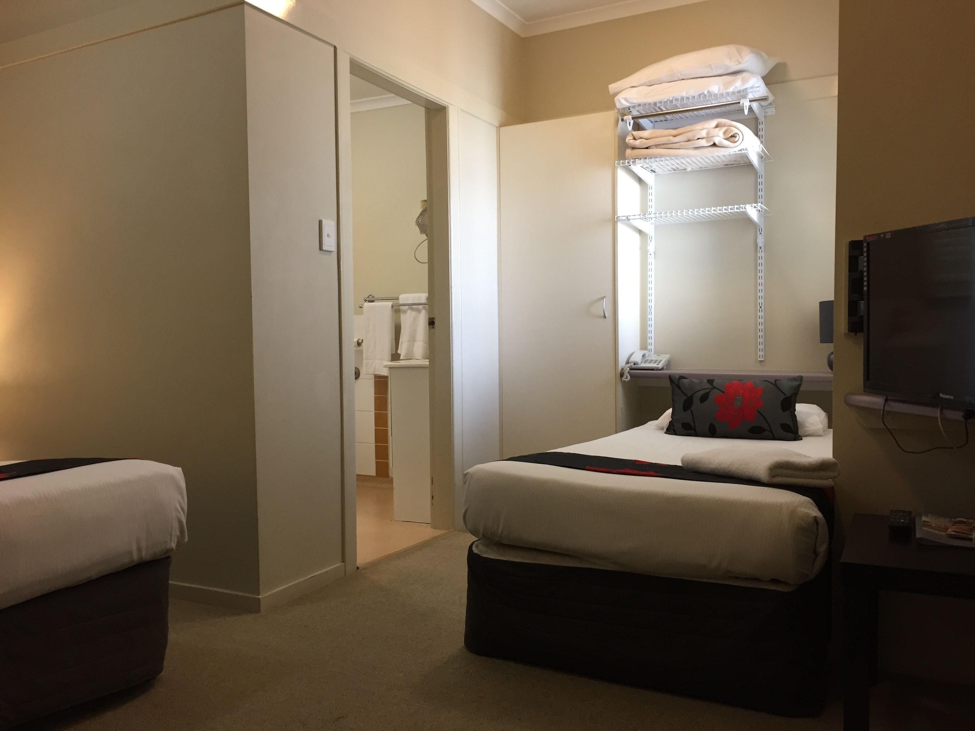 A hotel room with a bed, a TV, a desk, and a bathroom visible through an open door.