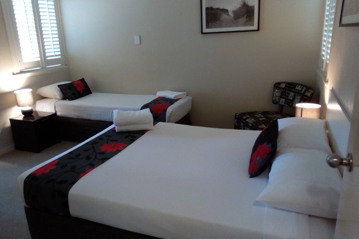 Habitación de hotel con dos camas, una mesita, una silla, una lámpara y un cuadro en la pared.