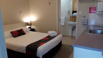 Une chambre d’hôtel comprenant un lit, une table de chevet, une lampe et une petite kitchenette équipée d’un évier et d’un plan de travail.