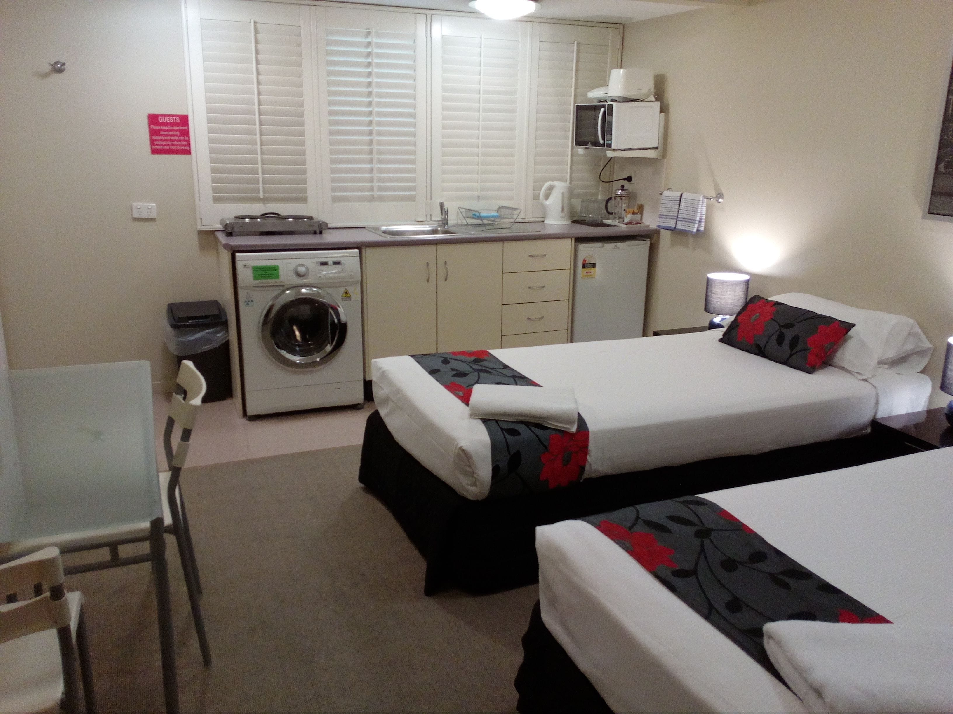 Una habitación de hotel con dos camas, lavadora, kitchenette pequeña y escritorio.