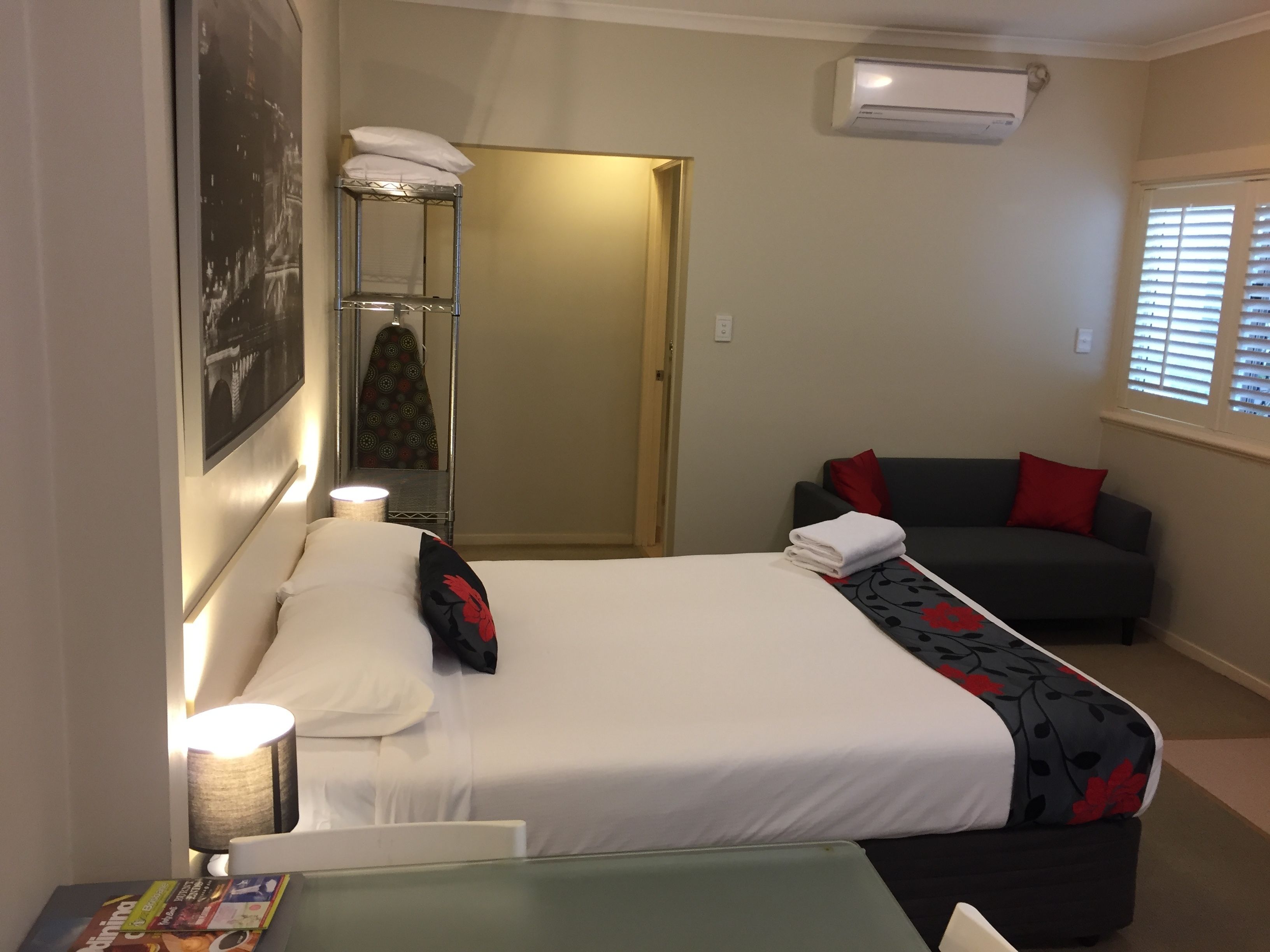 Une chambre d’hôtel équipée d’un lit, d’un canapé, d’une lampe, d’un climatiseur et d’une fenêtre avec des stores.