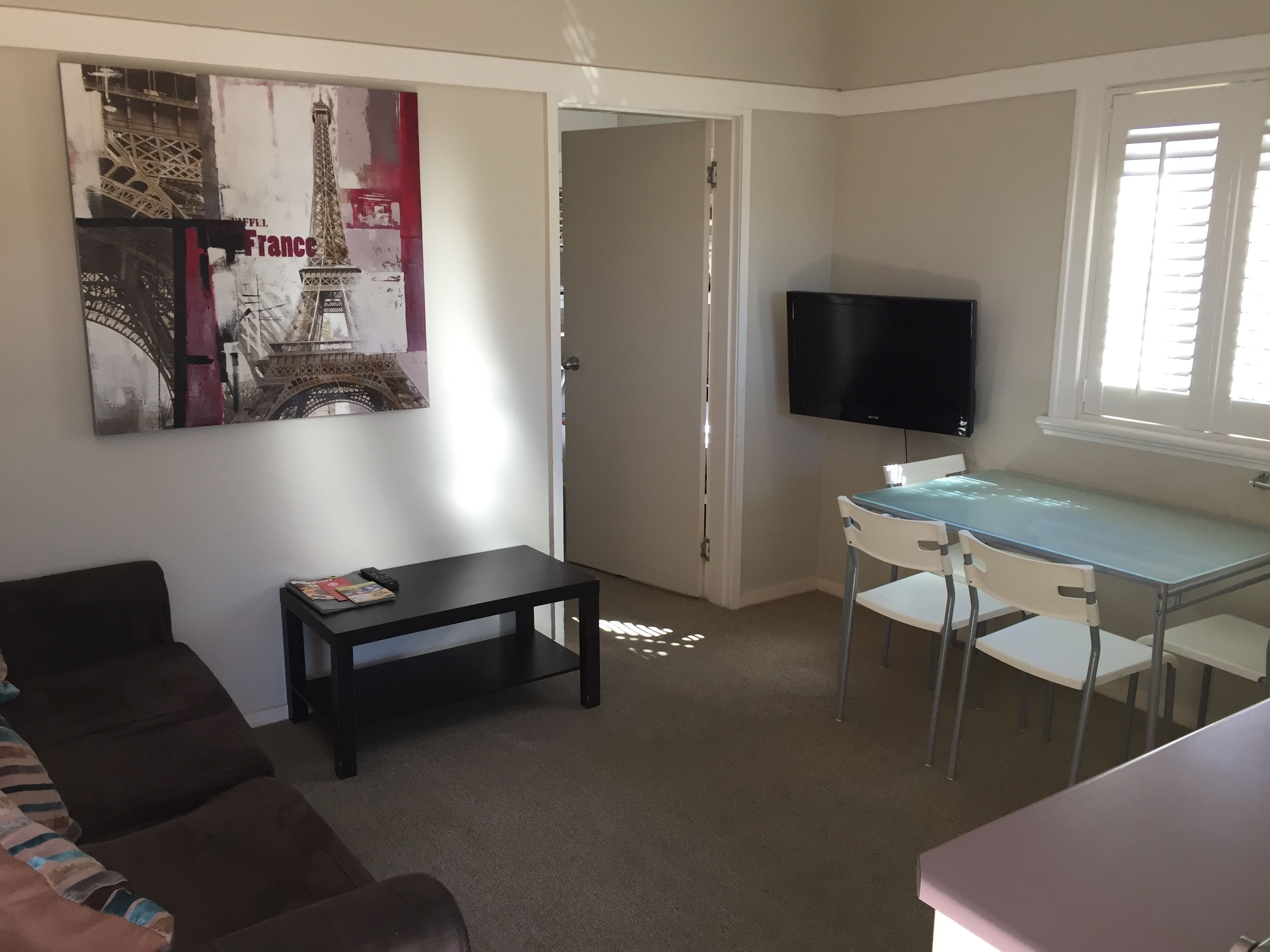 Una stanza piccola e luminosa con un letto singolo, una scrivania con un computer, una TV e un grande poster della Torre Eiffel.