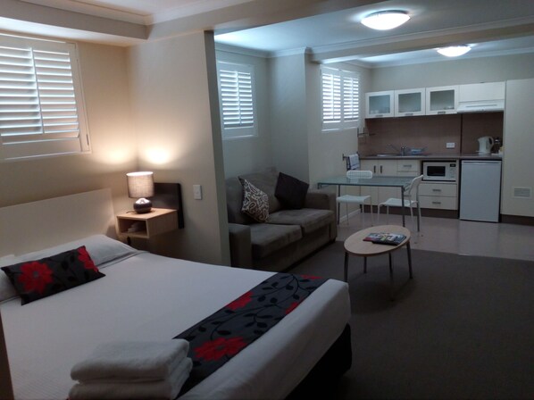 A hotel room with a bed, a desk, a kitchenette, and a sofa.