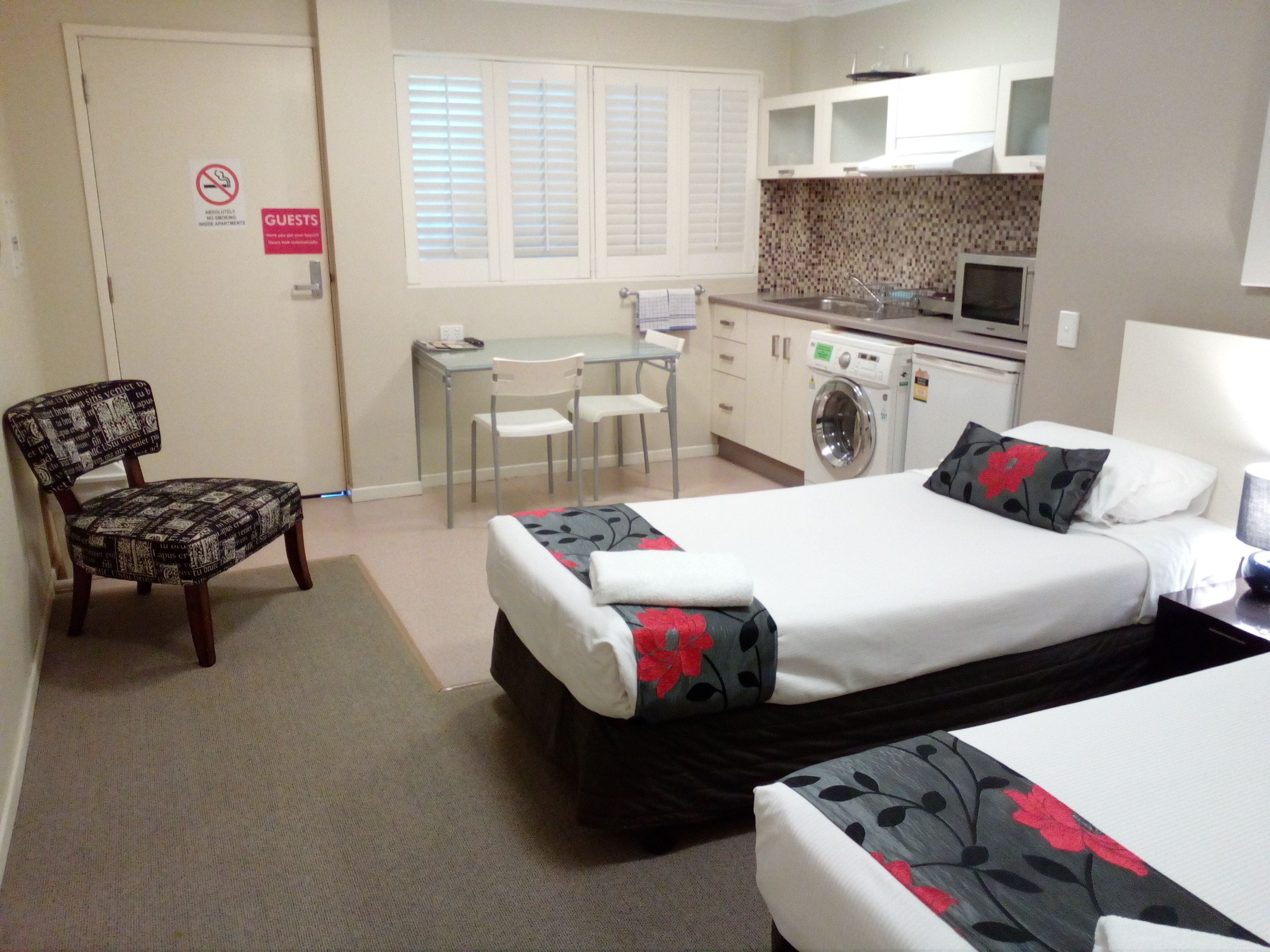 A compact hotel room with a bed, a chair, a desk, and a washing machine.