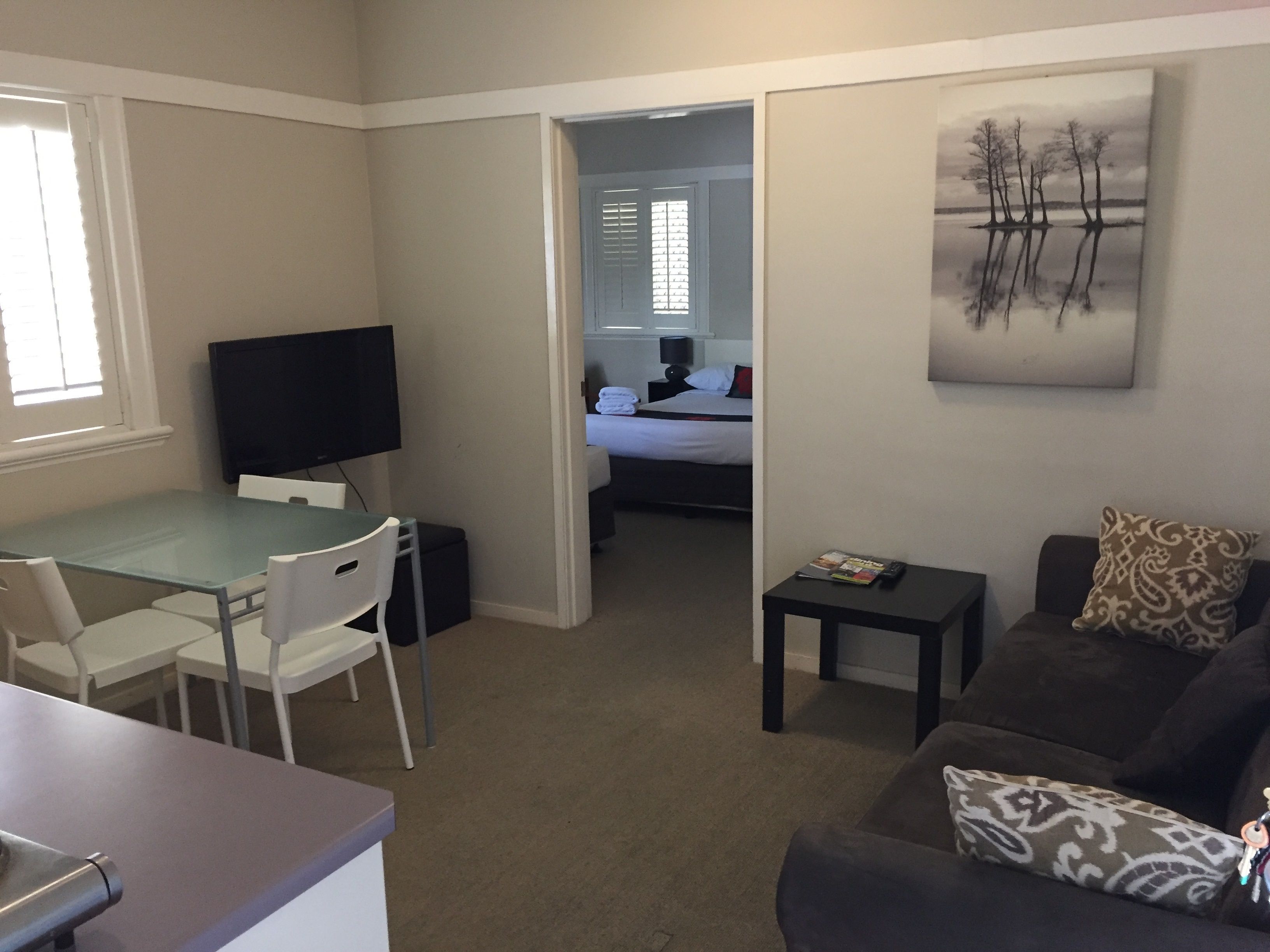 A compact living space with a dining area, a sofa, a TV, and a bed in the background.