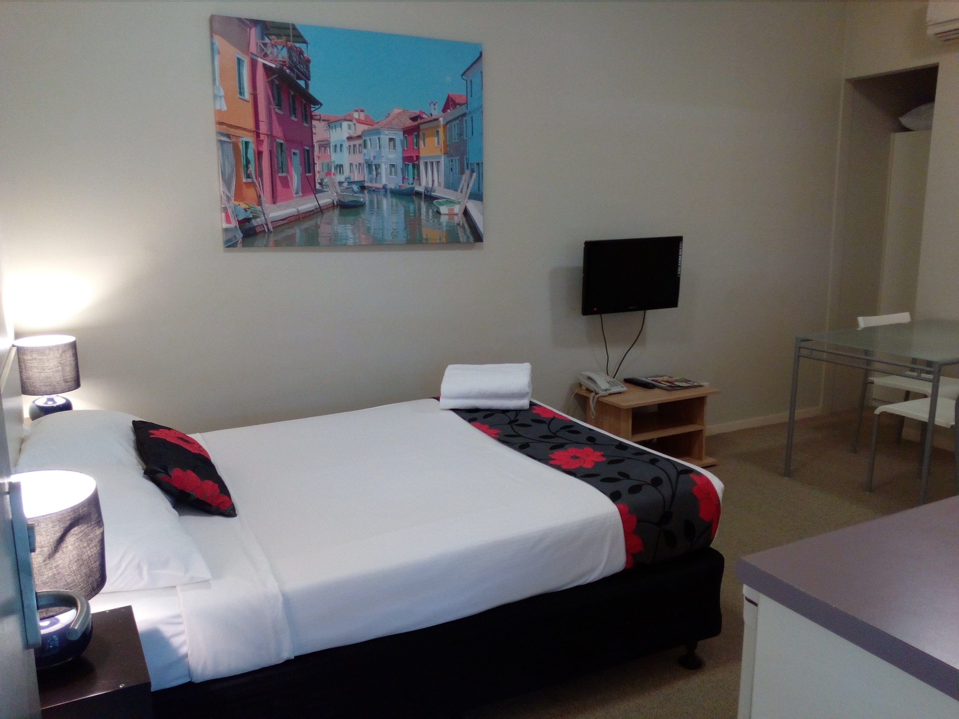 A hotel room with a bed, a desk, a chair, a TV, and a painting on the wall.