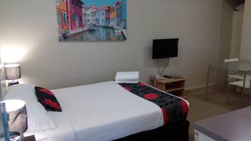 A hotel room with a bed, a desk, a chair, a TV, and a painting on the wall.