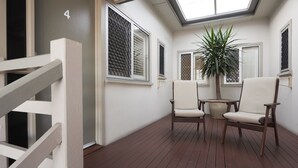 A sunlit room with a wooden floor, white walls, and a skylight. There are two chairs and a potted plant. - Brisbane Street Studios (Annerley)