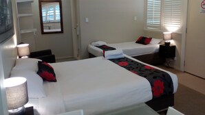 A hotel room with two beds, a desk, a chair, a lamp, a mirror, and a door with a sign. - Brisbane Street Studios (Annerley)