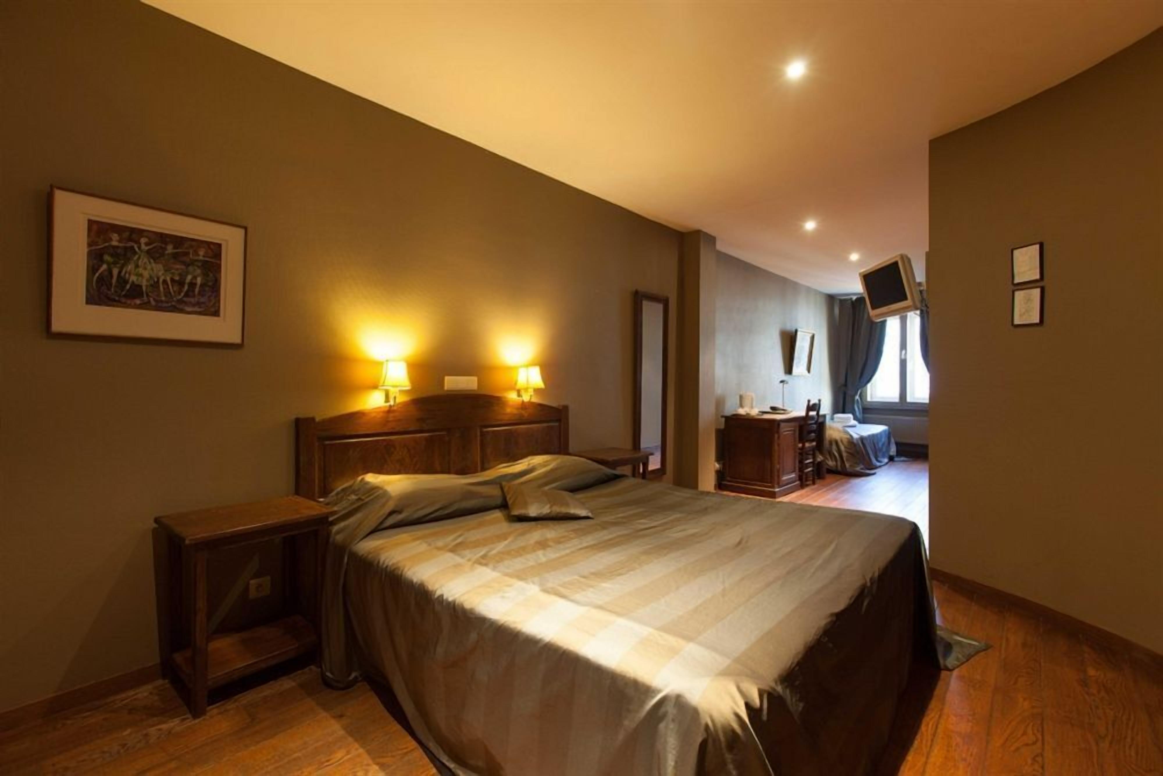 A hotel room with a large bed, bedside lamps, a wooden nightstand, a framed picture on the wall, and a television mounted on the wall.