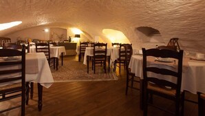 Un comedor subterráneo con mesas y sillas de madera, manteles blancos y un techo rústico de piedra.