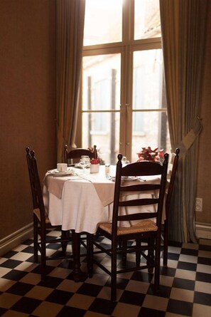 A dining table with a white tablecloth, wooden chairs, and a window with curtains. - Hotel Boterhuis (Bruges)