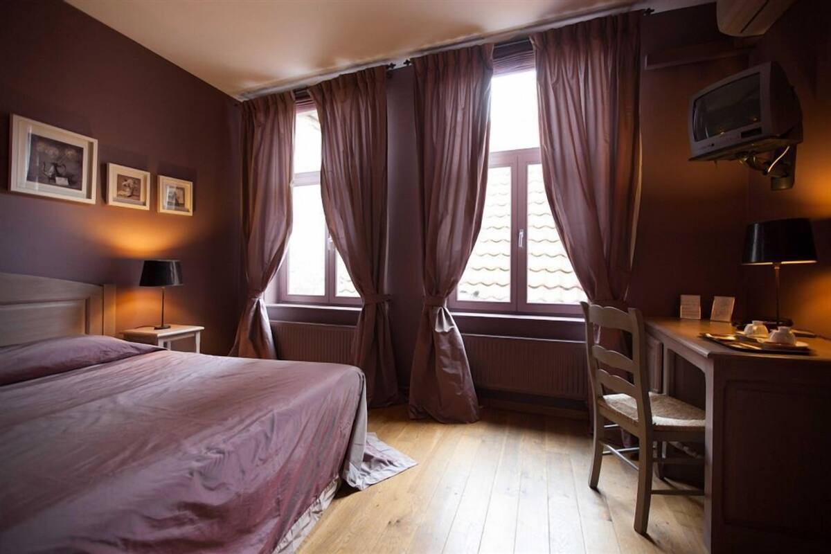 A bedroom with a bed, a desk, a chair, a TV, and curtains.