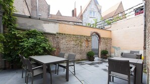 Un patio al aire libre con una mesa y sillas, rodeado de muros de ladrillo y una reja.