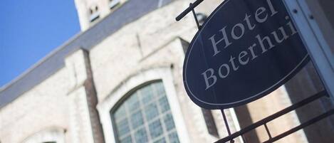 A hotel sign with the name "Hotel Boterhuis" against a building with large windows and a tower.