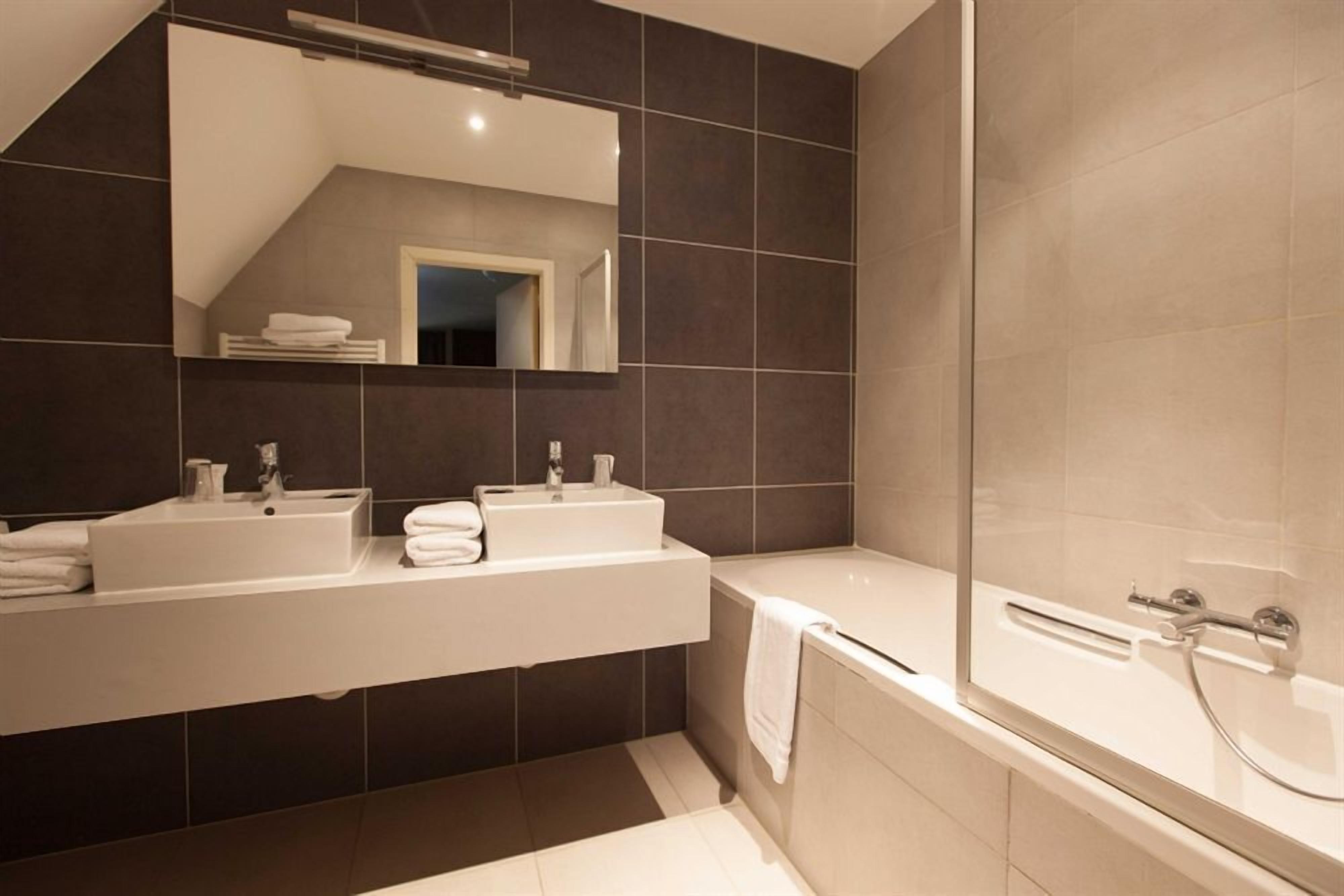 A modern bathroom with two sinks, a large mirror, and a bathtub.