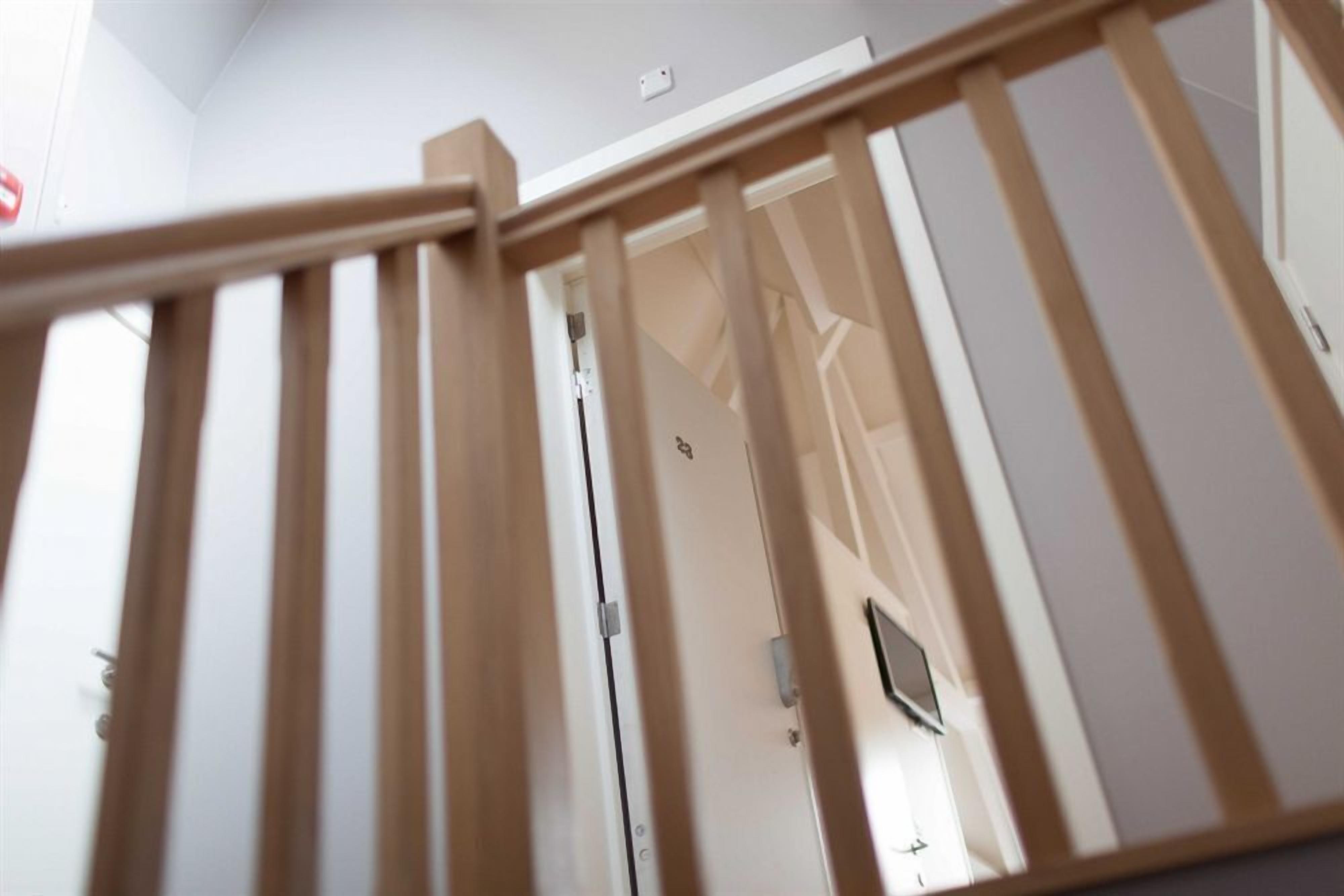A wooden staircase with a handrail leading to a room with a door and a light switch on the wall.